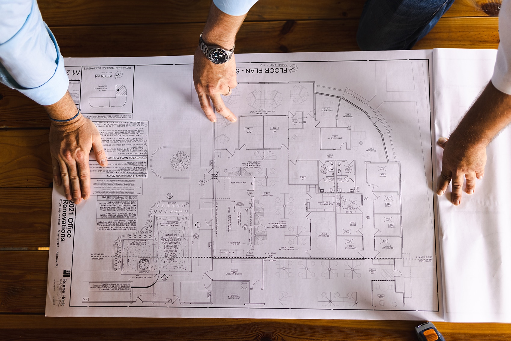 birds-eye-view of construction plan on paper with three hands on the plan