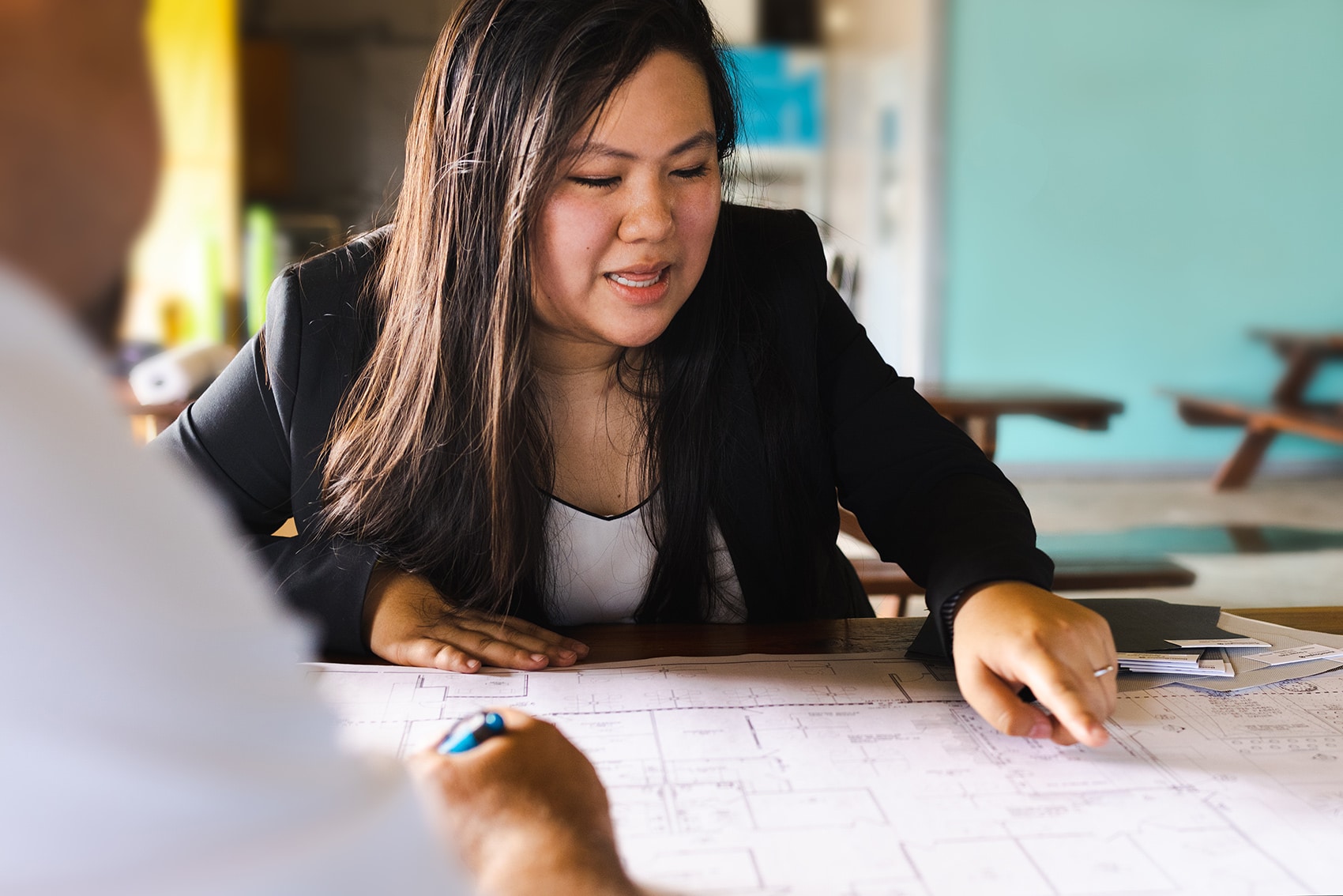 woman in business suit sitting at table pointing to construction plans