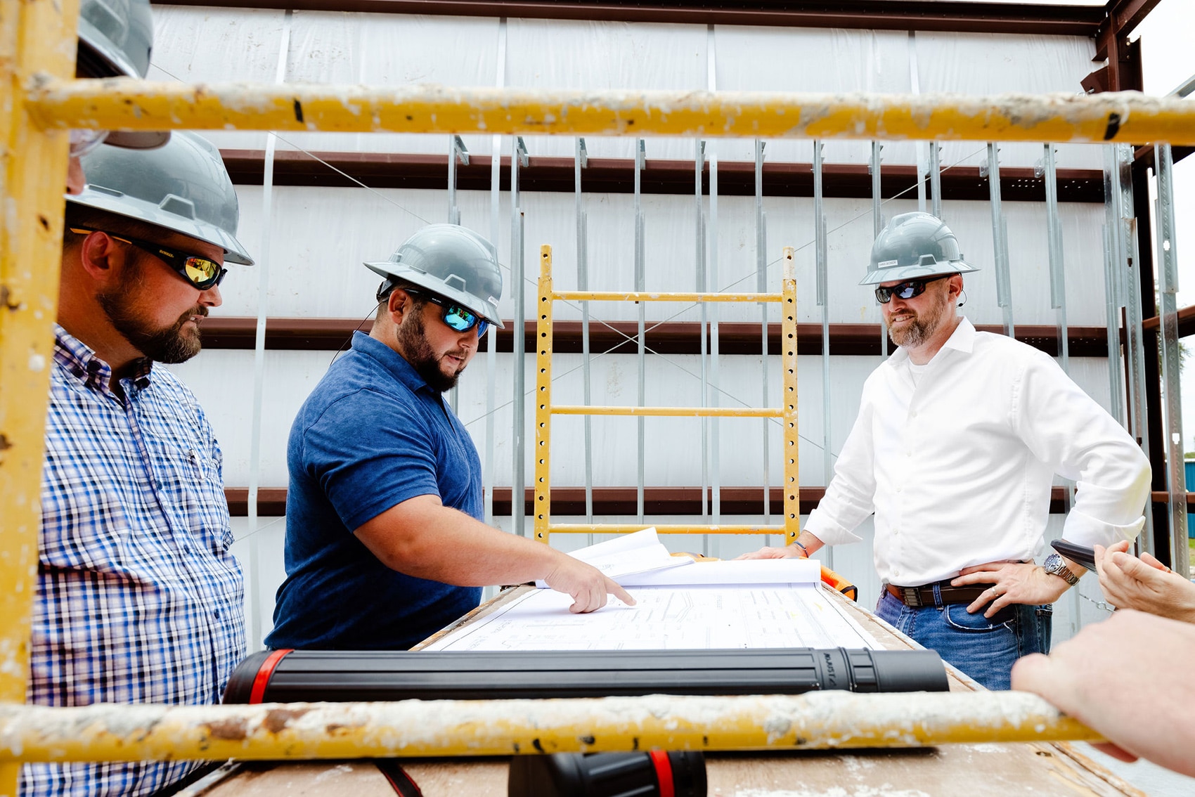 three men wearing construction hats on construction site looking at building plans