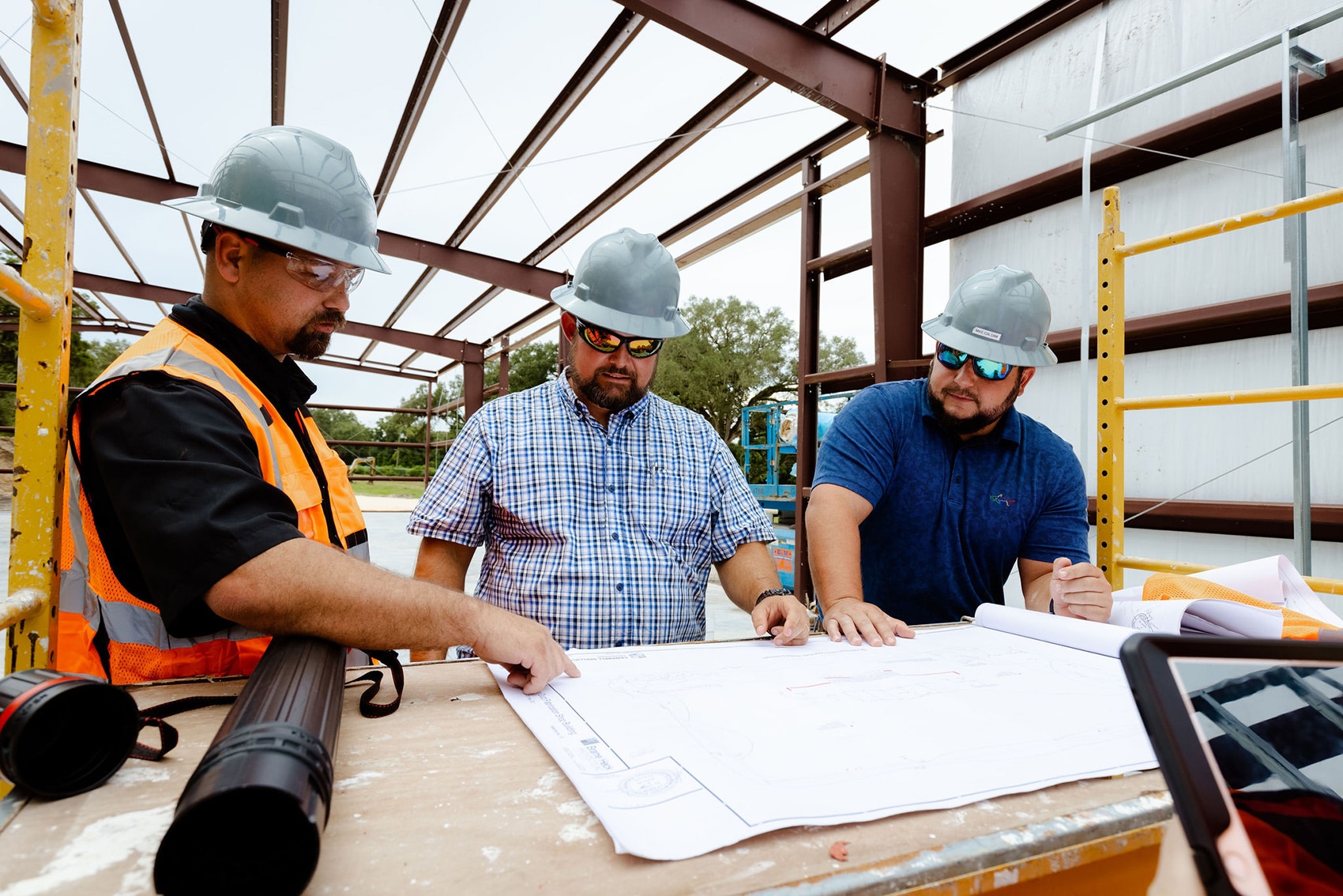 3 men wearing construction hats and sunglasses on construction site